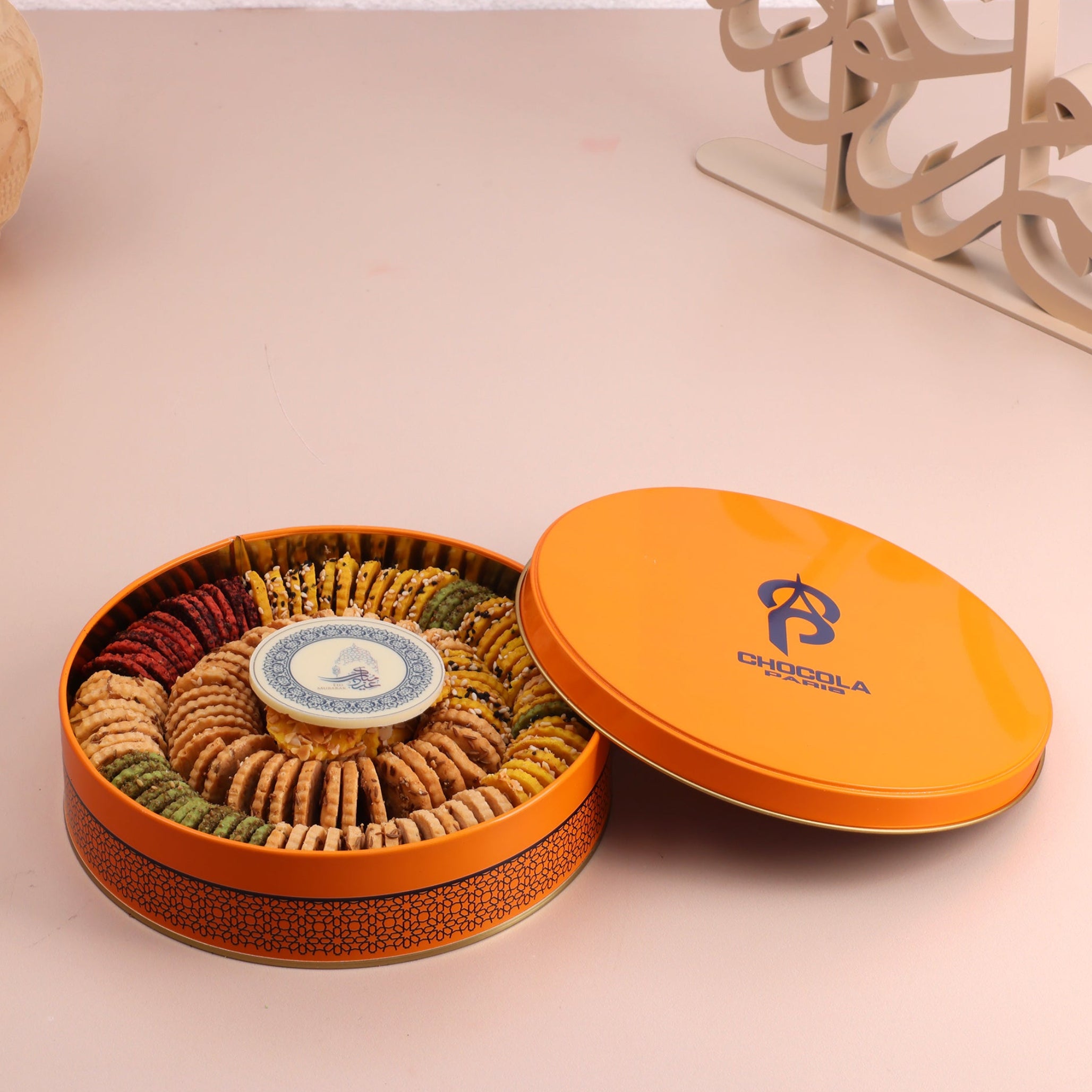 Open cookie tin with cookies inside on a light pink surface